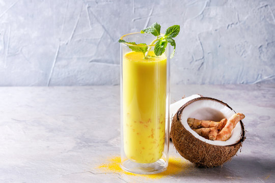 Cup Of Ayurvedic Drink Golden Coconut Milk Turmeric Iced Latte With Curcuma Powder, Crushed Ice, Mint And Ingredients Above Over Grey Kitchen Table. Copy Space