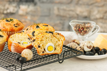 Savory muffins with olives, quail eggs and herbs on a wire rack on a white stone backdrop. Rustic style.