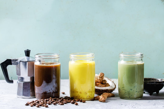 Variety of iced colorful latte drinks. Iced coffee, turmeric and matcha latte cocktails in glass jars with ingredients above over grey green texture background. Copy space