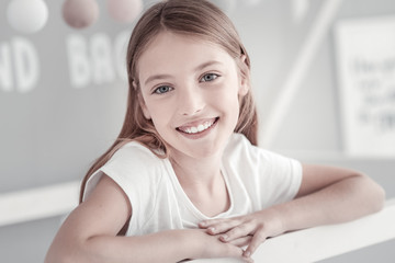 Naklejka premium In high spirits. Good-looking long-haired grey-eyed girl smiling and emitting happiness with her smile while wearing a white t-shirt