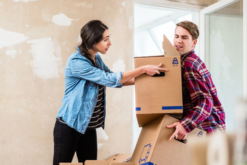 Young woman helping her partner to carry two heavy cardboard boxes while moving in into a new home 