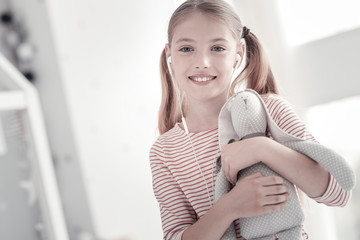 My favourite toy. Good-looking cheerful lovely girl with pig-tails smiling and holding a toy while wearing a striped dress and a headset