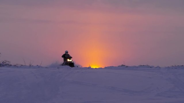A snowmobile is riding at sunset