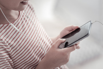 Using my phone. Smiling girl wearing a striped dress and a headset and holding her phone while listening to the music