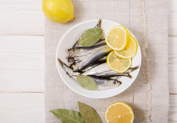 Salted sprat with spice and lemon on the white plate.Wooden table with coarse tablecloth.