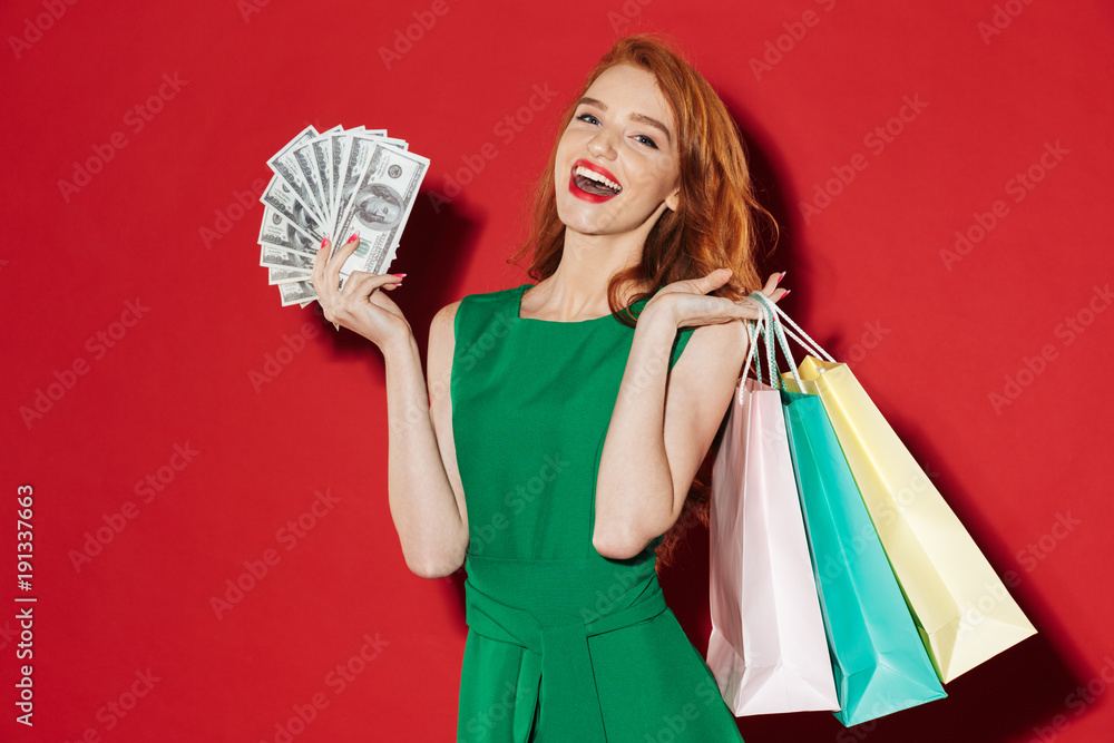 Poster Young redhead happy girl with money and shopping bags