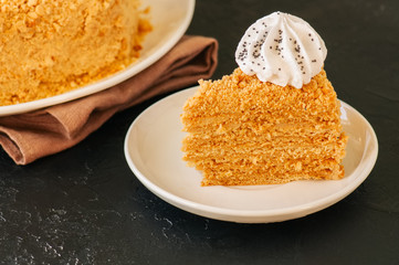 Honey cake with meringue decoration on top served on a white plate on a black backdrop.