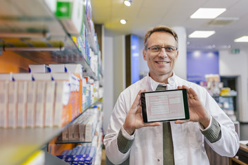 Portrait of smiling pharmacist in pharmacy holding tablet with digital prescription
