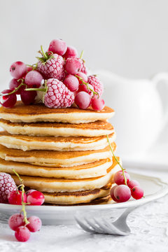 Stack of pancakes with raspberry, red currant, cream and honey on white table cloth