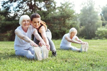 Fototapeta premium Professional trainer. Delighted well built young woman smiling and assisting her client while showing how to do the exercise