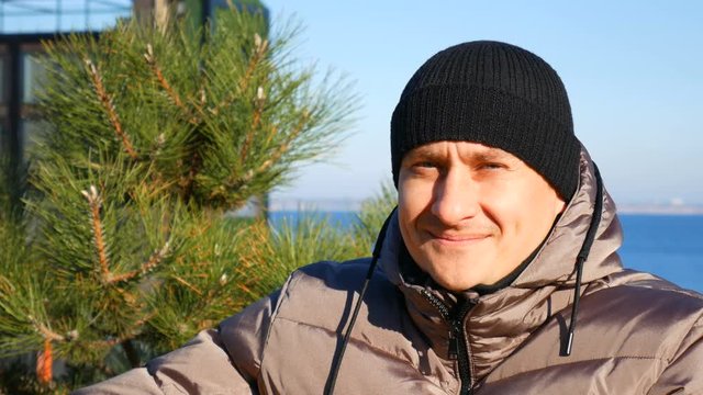 Closeup portrait of smiling caucasian man against the background of a pine tree park and the sea