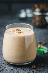 Coffee banana smoothie and coffee beans in glass jar on dark concrete background. Selective focus, space for text. 