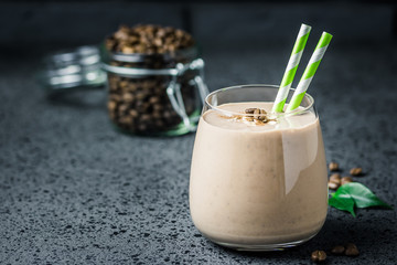 Chocolate mocha breakfast smoothie and coffee beans in glass jar on dark concrete background. Selective focus, space for text. 