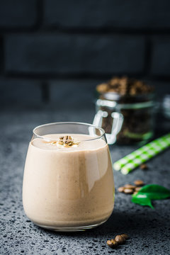 Banana chocolate espresso coffee smoothie and coffee beans in glass jar on dark concrete background. Selective focus, space for text.