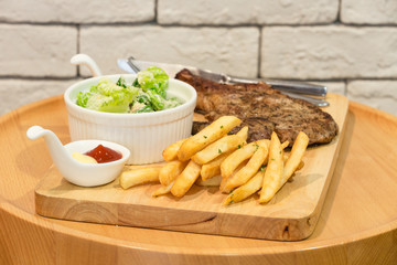 Plate of grilled pork with French fries and salad on wooden background