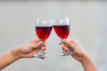Clinking glasses of red wine in hands on nature lights background