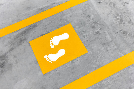 Walkway lane in parking building. Painted yellow footsteps between parallel yellow lines on abstract cement floor.