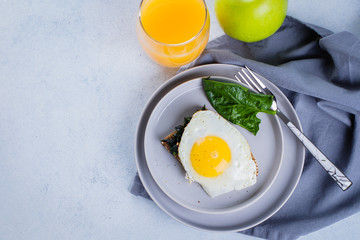 Rye bread toasts with fried spinach and egg with glass of orange juice and green apple on blue table background. Healthy Breakfast Food Concept. Top view with copy space