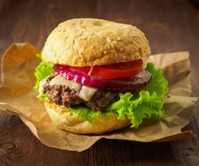 Big delicious homemade burger with beef cutlet, cheese, onion, tomato and lettuce on toasted rolls. American fast food, unhealthy eating.  Side view, selective focus