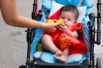 Close up of Chinese baby receiving orange, Chinese traditional in Chinese new year for Lucky, from parent in perambulator baby stroller..