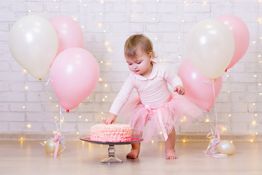 birthday celebration - funny little girl smashing cake over brick wall background with lights and balloons