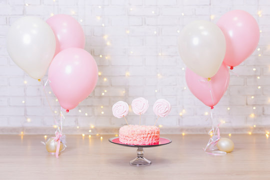 birthday celebration concept - cake over brick wall background with lights and balloons