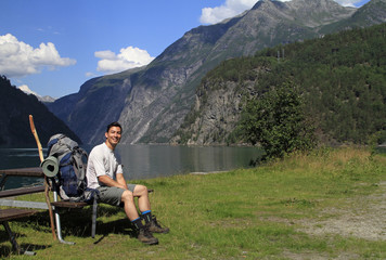 Hiker with backpack taking a break next to a beautiful fjord in Norway