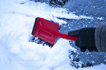 Person fegt Schnee von Windschutzscheibe eines Autos im Winter ab, Wintereinbruch