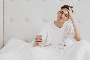 Handsome young man in pajamas using a cellphone while lying in bed in the morning. Copy space.