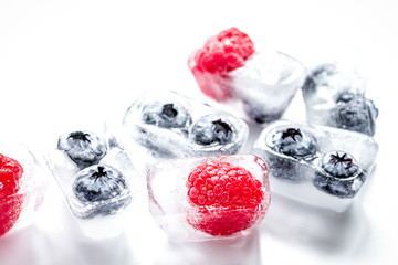 frozen blueberry and raspberry in ice cubes on white background