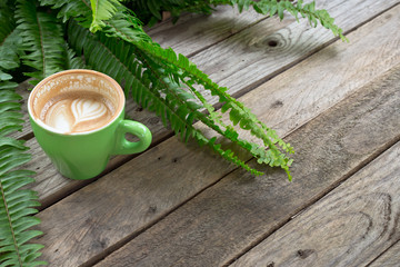 coffee cup on wood table with fern leaf background
