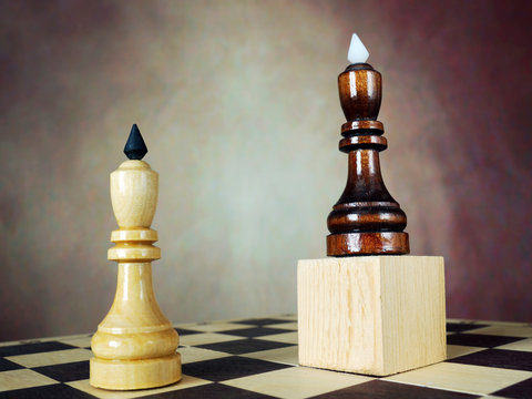 Superiority. Concept with chess pieces. One chess king has an advantage over another because he stands on a wooden stand