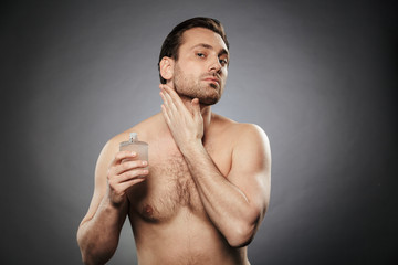 Portrait of a handsome shirtless man using aftershave lotion