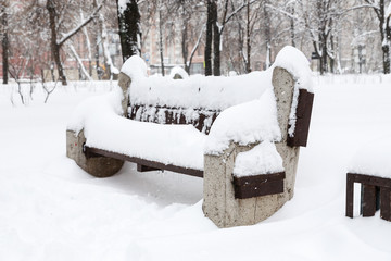 Snow covered bench among snowbanks in city park