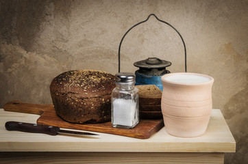 Milk in a clay pot, rye bread, salt in a salt shaker on a cutting board. Still-life in the rustic style