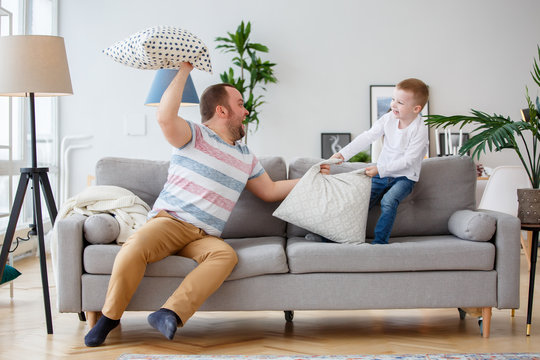 Image of father fighting with son cushions on gray sofa
