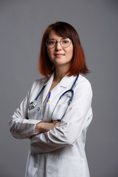 Image of smiling female doctor in white lab coat and with phonendoscope in glasses