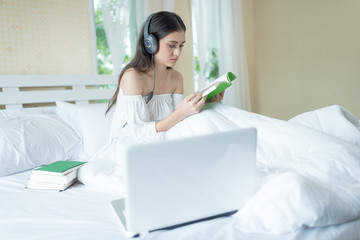 Obraz na płótnie Canvas Charming woman on bed wearing headphone enjoy music and reading book at weekend