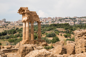 Fototapeta premium The re-assembled remains of the Temple of Castor and Pollux with Agrigento city in the background. Valle dei Templi - temples Valley, Agrigento, Italy.