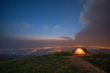 Fototapeta na wymiar Illuminated orange camping tent on the hill with city light background