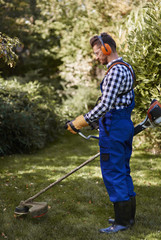Busy man using a weedwacker at garden