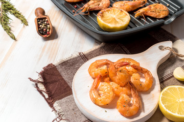 Grilled shrimps with lemon, paprika, spices and herbs on a white wooden board.