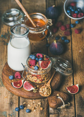 Healthy vegan breakfast. Oatmeal granola with bottled almond milk, honey, fresh fruit and berries on hoard over rustic wooden table background. Clean eating, weight loss, vegetarian food concept