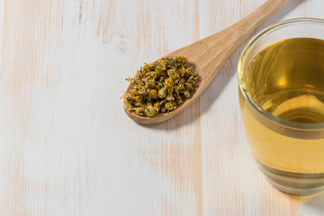 Cup of chamomile tea with dry chamomile flowers  on white wooden background.