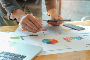 Man hand holding pen pointing to graph on desk,other hand uses a tablet,Business concepts.