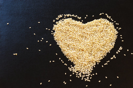 White sesame seeds arranged in heart shape on black background. Copy space.