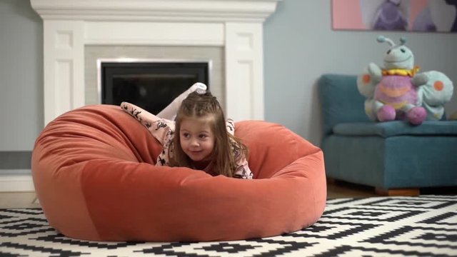 Portrait of energetic little girl 5-6years having fun, playing and jumping on bean bag chair in cozy children room in slow motion