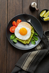 Fried egg with cheese, tomatoes, chard, and waffle with spinach on black ceramic plate on brown old wooden background. Sandwich for breakfast. Selective focus. Top view. Copy space.