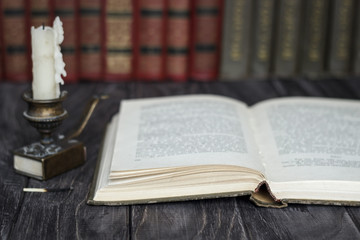 On the wooden background of the table there are stacks of colorful books near the old candlestick with burnt matches lying next to each other.