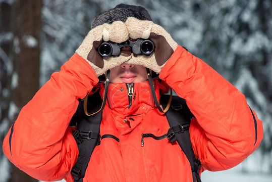 man with binoculars looking at camera, shooting in winter forest